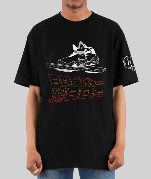 A man wearing a black t-shirt featuring a hand-illustrated design inspired by the movie Back to the Future, showcasing iconic elements like the Hoverboard and time-travel details.