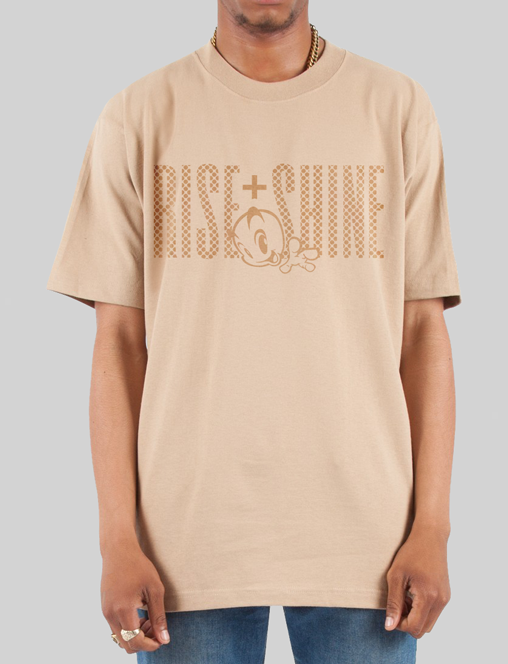 A front view of a man wearing a tan t-shirt featuring a subtle 'Rise and Shine' design with a stylized checkered graphic and uplifting text.