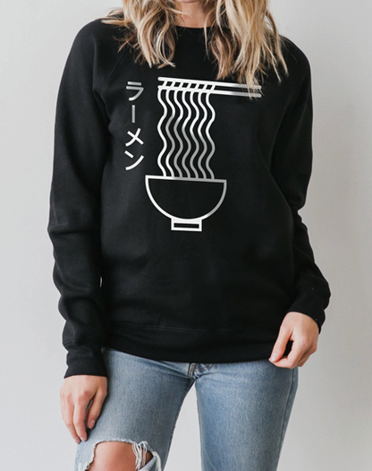 A woman with blonde hair wearing a black sweatshirt featuring a detailed, hand-illustrated design of a steaming bowl of pho noodles with chopsticks, capturing the essence of the popular dish.